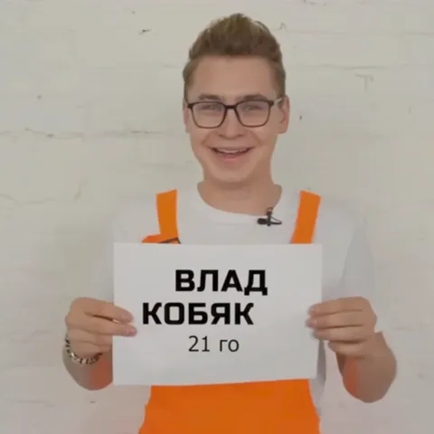 Улыбающийся парень в очках и оранжевой одежде показывает лист бумаги с текстом «ВЛАД КОБЯКОВ 21 год».