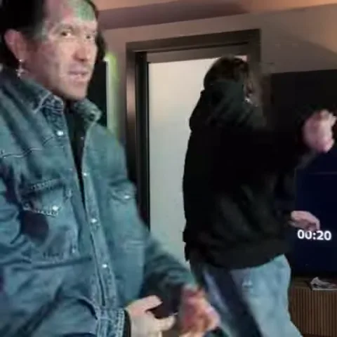 Мужчина с татуировками на лице в джинсовой куртке танцует с группой друзей в помещении с фиолетовым освещением