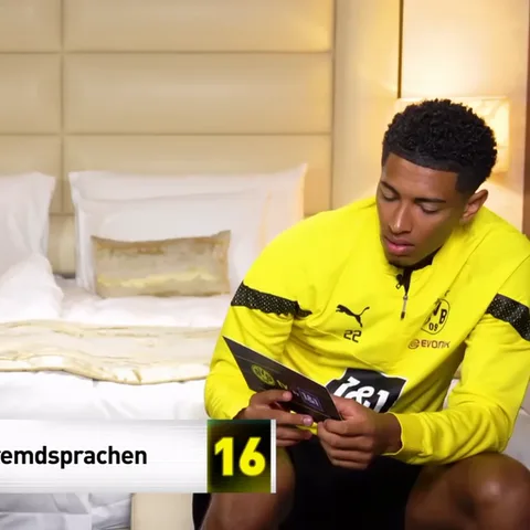 Молодой человек в спортивной куртке с логотипом Puma сидит на кровати и внимательно смотрит на темную карточку в своих руках.