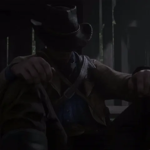 Анимация персонажа из игры Red Dead Redemption II: ковбой сидит на полу в полумраке, спрятав лицо под полями шляпы.