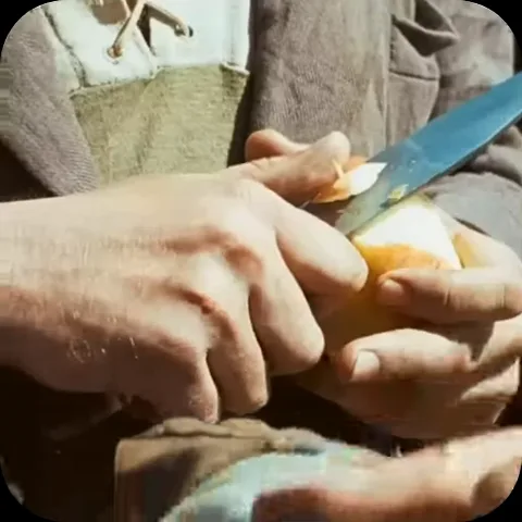 Мужские руки держат яблоко и аккуратно срезают с него кожуру ножом. На руке видны часы под тканью.