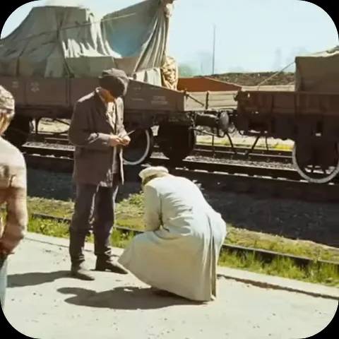 Анимация из сериала «Генеральские котлы»: мужчина в белом пальто приседает на корточки перед мужчиной в темном костюме на фоне товарных вагонов.