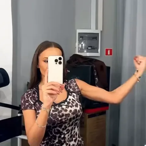 Брюнетка в леопардовой футболке фотографируется на телефон и сгибает руку, показывая мышцы.