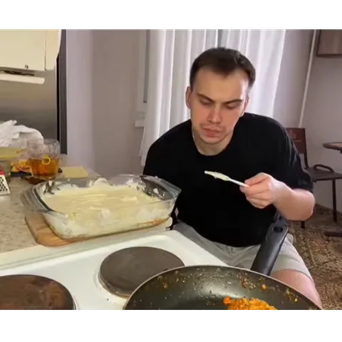 Мужчина сидит на кухне, ест из большой стеклянной формы и облизывает ложку.
