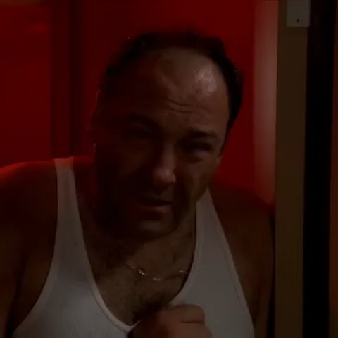 Мужчина в белой майке с обеспокоенным выражением лица на фоне красного света.