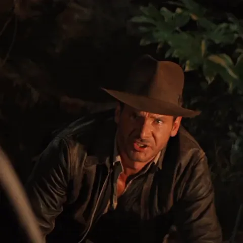 Индиана Джонс отмахивается рукой от огня у костра.